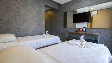 Quarto de hotel com duas camas, televisão de tela plana na parede e uma mesinha com chaleira e xícaras.