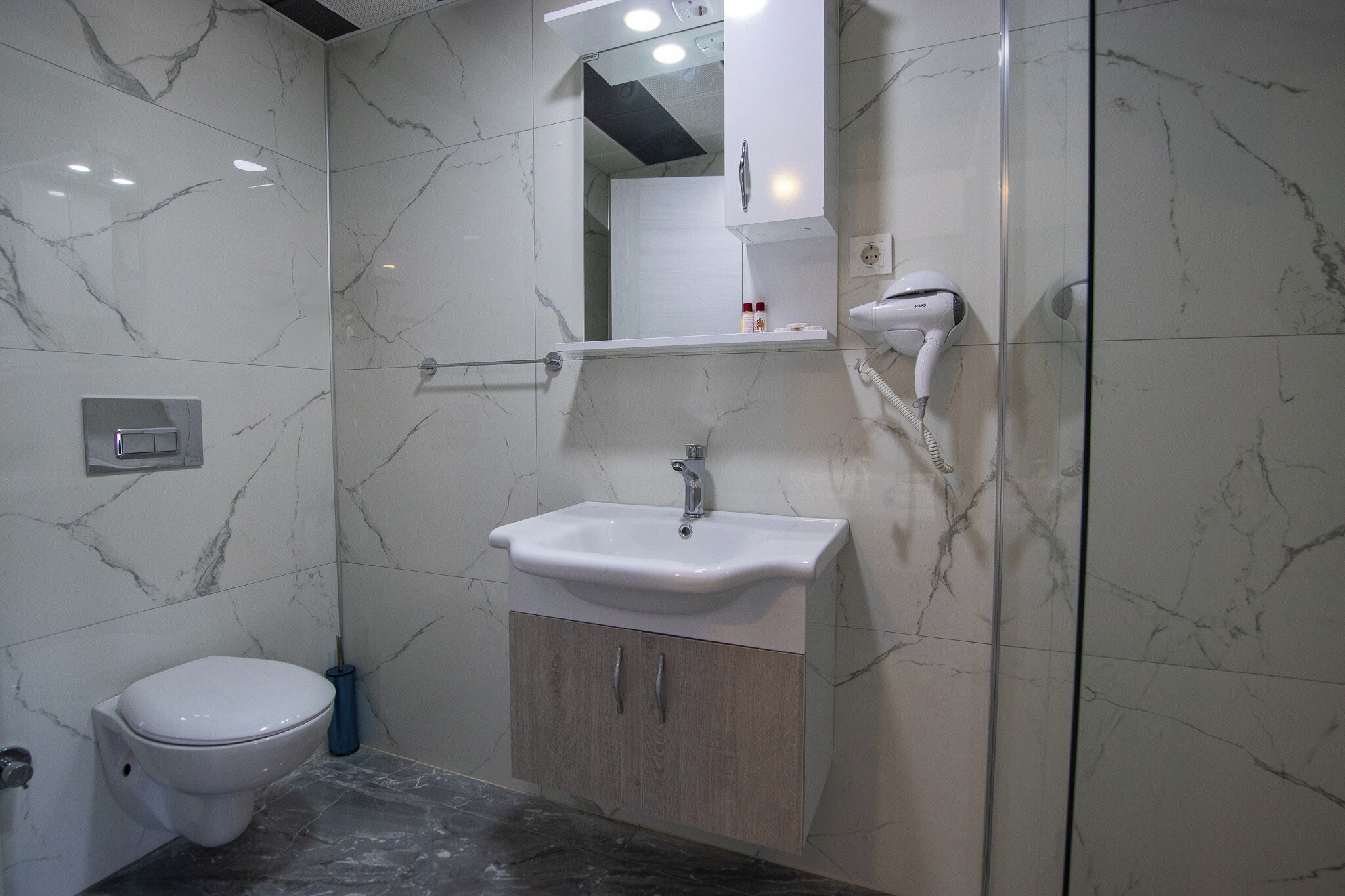 A bathroom with a white toilet, a sink with a mirror above it, and a hairdryer on the wall.
