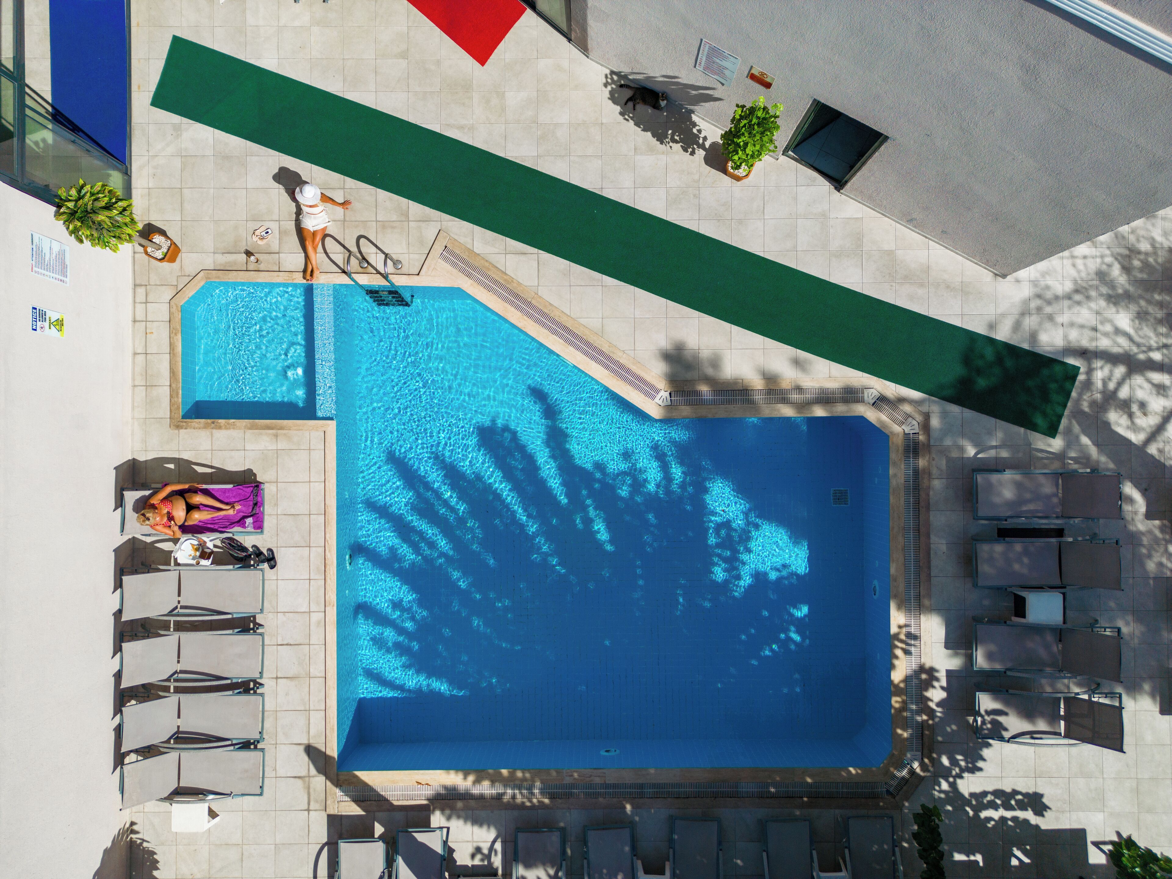 Vista aérea de uma piscina com espreguiçadeiras, um solário e uma pequena área de jardim.