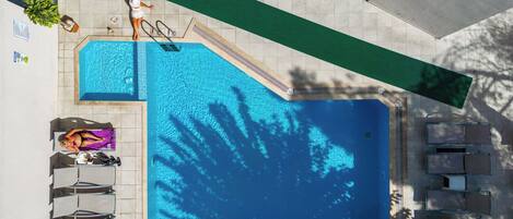 Vista aérea de uma piscina com espreguiçadeiras, um solário e uma pequena área de jardim.