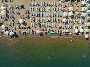 An aerial view of a beach with rows of sun loungers and umbrellas, a clear view of the ocean, and a few people in the water. - Emilia Hotel (Marmaris)