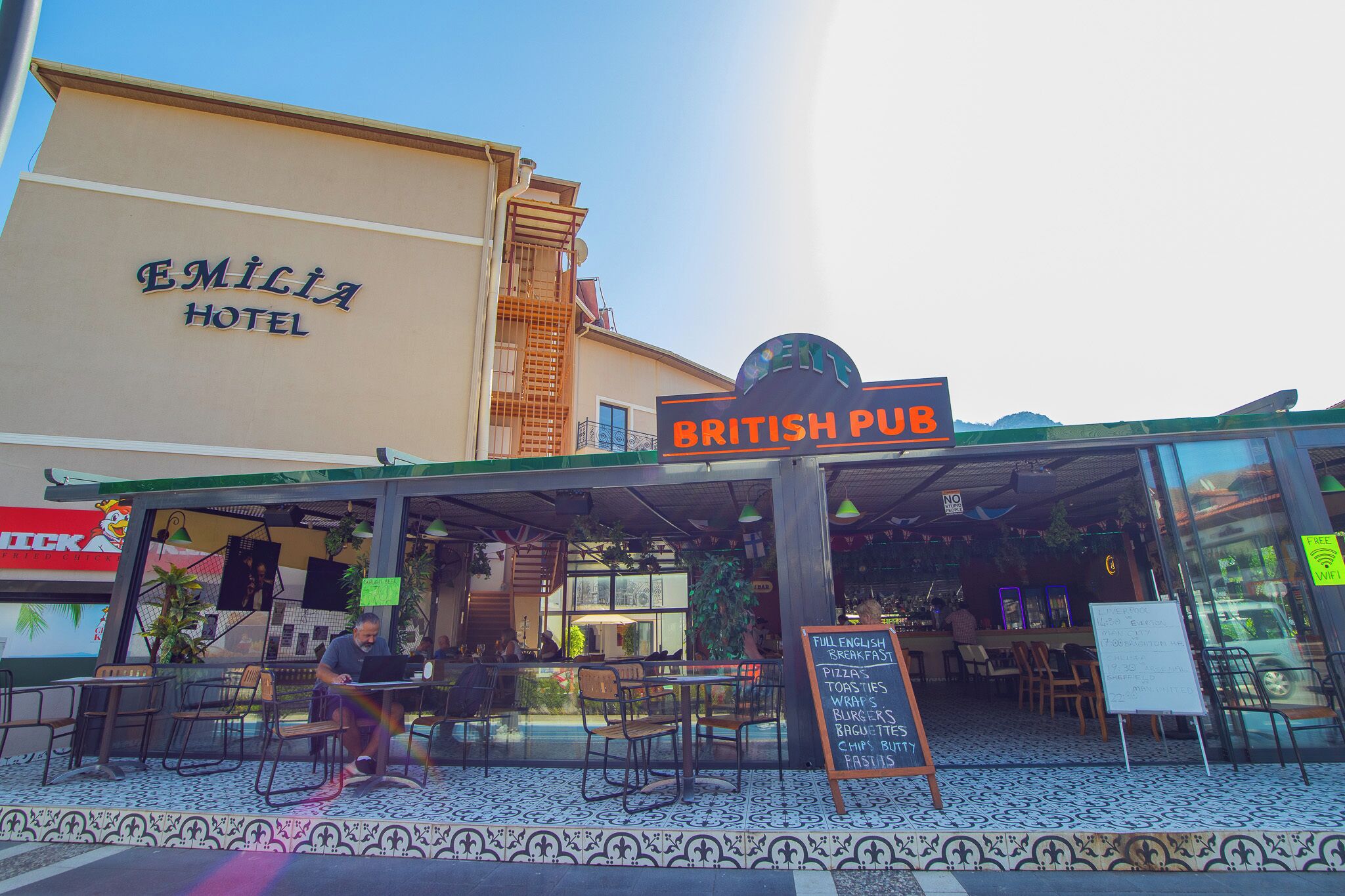 A British Pub with outdoor seating, a signboard for full English breakfast, and a visible hotel in the background.