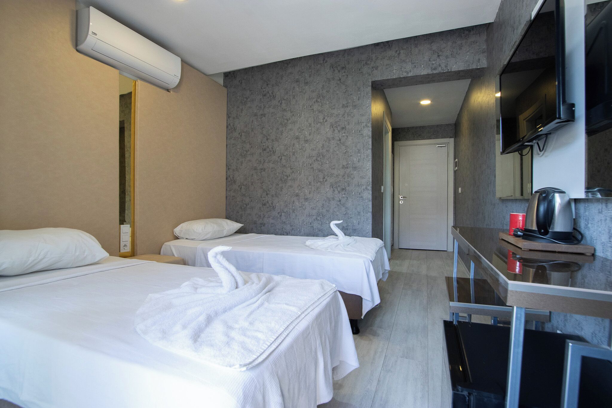 Habitación de hotel con dos camas, un escritorio con hervidor y televisor.