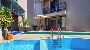 Una piscina con escalera, rodeada de plantas en macetas y mobiliario de exterior.
