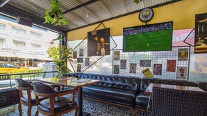 Un rincón de bar acogedor con un sofá de cuero negro, sillas de madera y suelo de baldosas.