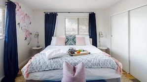 Quarto com cama, cortinas, mesa de cabeceira, persianas na janela e parede com um desenho floral.