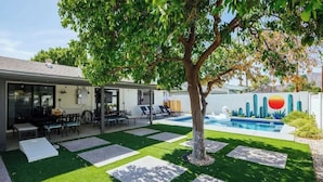 Quintal com piscina, uma árvore e área de estar com móveis de exterior.