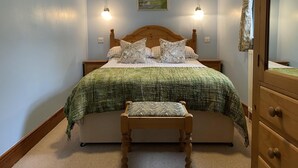 A bedroom with a bed, two bedside tables, a wooden bench, a painting on the wall, and a mirror on the door.