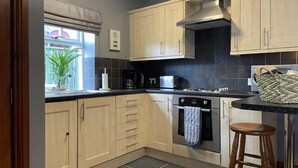 A compact kitchen with light wood cabinets, a black tiled backsplash, a built-in oven, and a coffee maker.