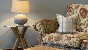 A living room with a glass coffee table, a sofa with floral upholstery, and a lamp on a wooden side table. - Milecastle Inn on Hadrian's Wall Near Haltwhistle (Haltwhistle)