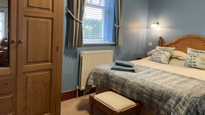 A bedroom with a wooden wardrobe, a bed with a patterned bedspread, a bench, and a window with curtains. - Milecastle Inn on Hadrian's Wall Near Haltwhistle (Haltwhistle)