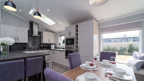 Een moderne keuken met witte kasten, een houten eettafel gedekt met borden en glazen, en uitzicht op de achtertuin door grote ramen.