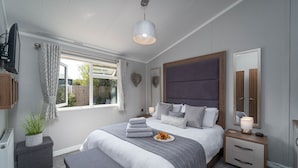 Een slaapkamer met een bed, nachtkastjes, een spiegel, een raam met gordijnen en een potplant.