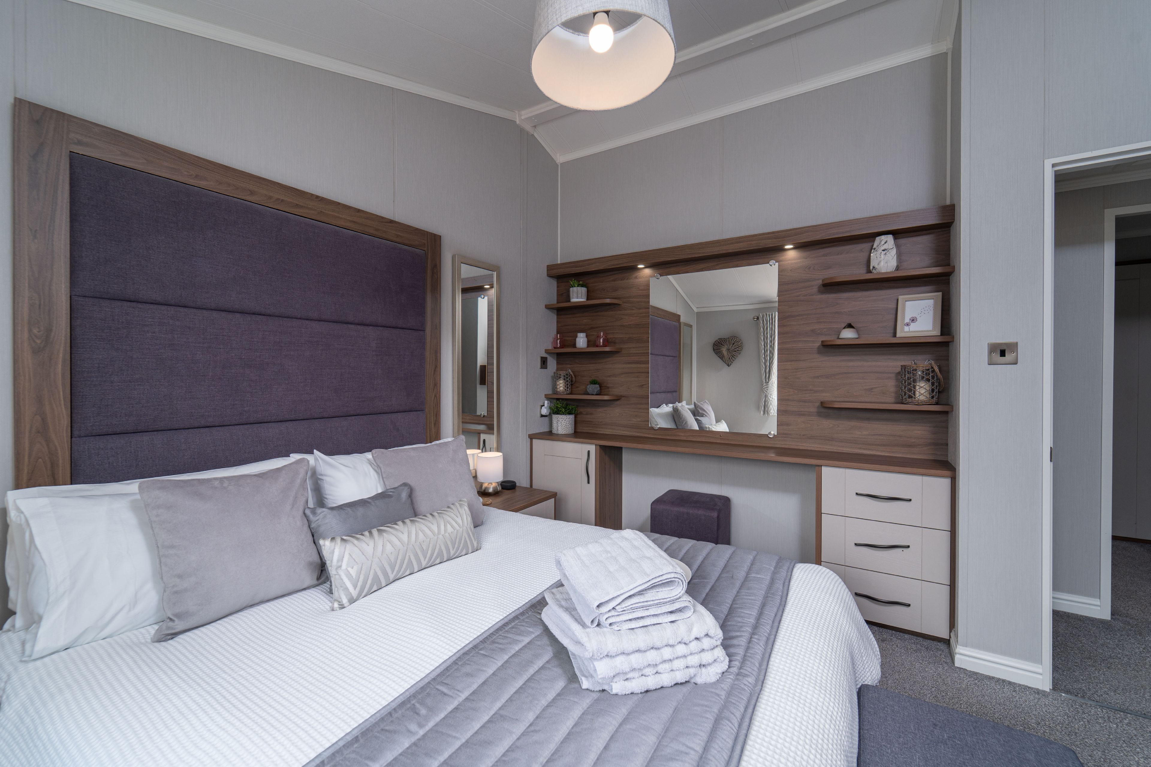 A modern bedroom with a large bed, a built-in wardrobe, and a vanity with a mirror.