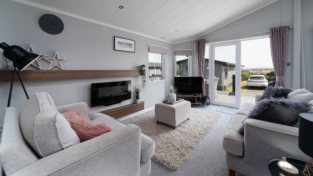 Een moderne woonkamer met een flatscreen televisie, twee banken, een salontafel en een groot raam met gordijnen.