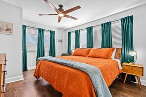 A bedroom with a bed, a nightstand, a ceiling fan, and green curtains.