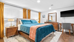 Quarto com cama, mesas de cabeceira, escrivaninha e televisão.