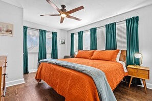 A bedroom with a bed, a nightstand, a ceiling fan, and a window with curtains.