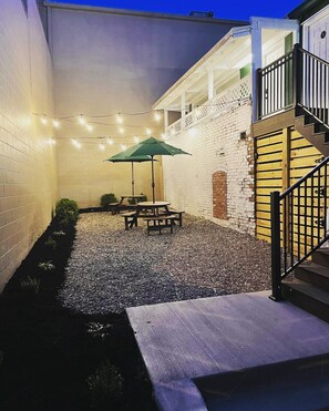 A patio with a table and chairs, a green umbrella, and string lights.