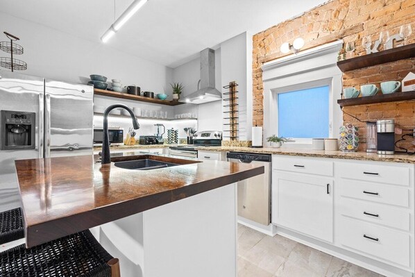 A modern kitchen with white cabinetry, a stainless steel refrigerator, and a brick accent wall.