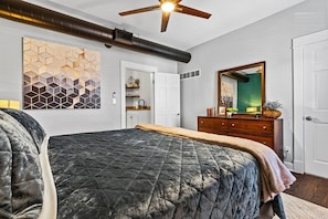 A bedroom with a large bed, a ceiling fan, a dresser, a mirror, and a geometric wall art piece. - Belvedere Flats - 2 units + Walkable to Westport! (Kansas City)