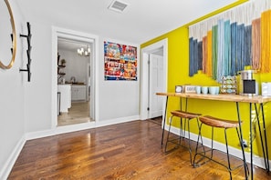 A modern kitchen with a yellow accent wall, a bar area with stools, and a visible doorway leading to another room. - Belvedere 1 | Modern 3-Bed Flat in Westport (Kansas City)