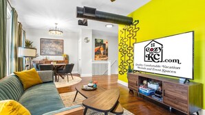 A modern living room with a sofa, a dining table, and a TV displaying a logo.