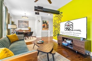 A modern living room with a sofa, a dining table, and a TV displaying a logo.