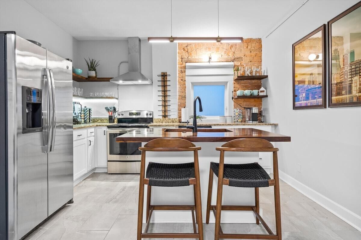A modern kitchen with stainless steel appliances, a central island, and two wooden bar stools.