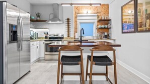 A modern kitchen with stainless steel appliances, a central island, and two wooden bar stools.
