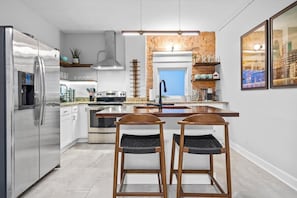 A modern kitchen with stainless steel appliances, a central island, and two wooden bar stools.