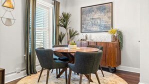 A dining area with a round table, four chairs, a wooden cabinet, and a cityscape painting on the wall.