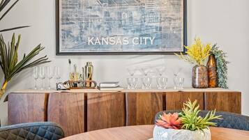 A dining area with a round table, chairs, a wooden cabinet with glassware, and a framed cityscape artwork.