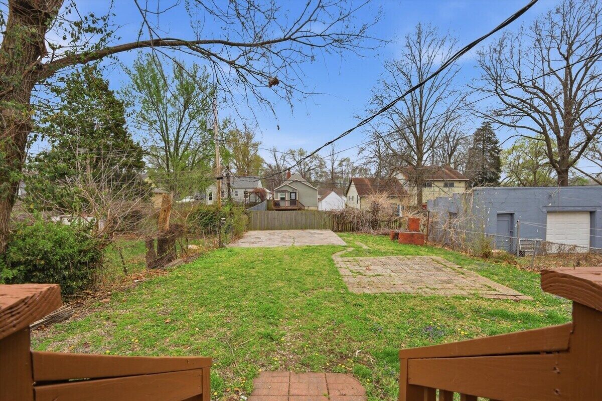 A backyard with a paved area, a wooden bench, and a house in the background.
