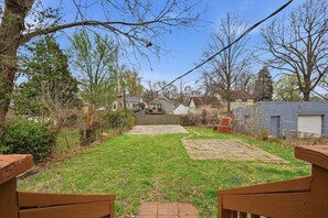 A backyard with a paved area, a wooden bench, and a house in the background.