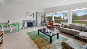 A modern living room with a fireplace, a dining area, and a sofa facing large windows.