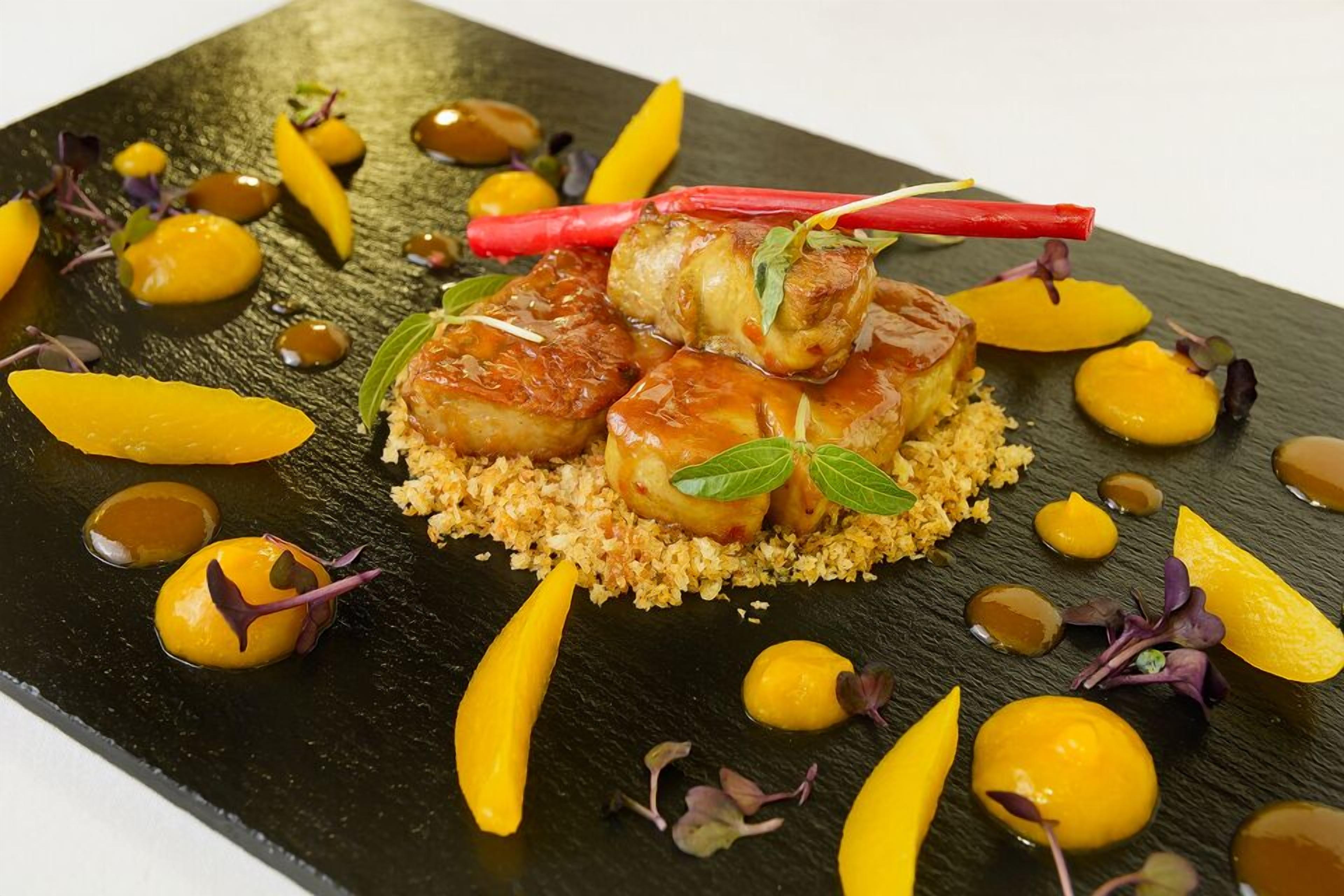 A plated dish with scallops, garnished with herbs and sauce, on a textured black plate.