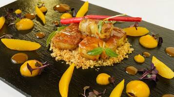 A plated dish with scallops, garnished with herbs and sauce, on a textured black plate.
