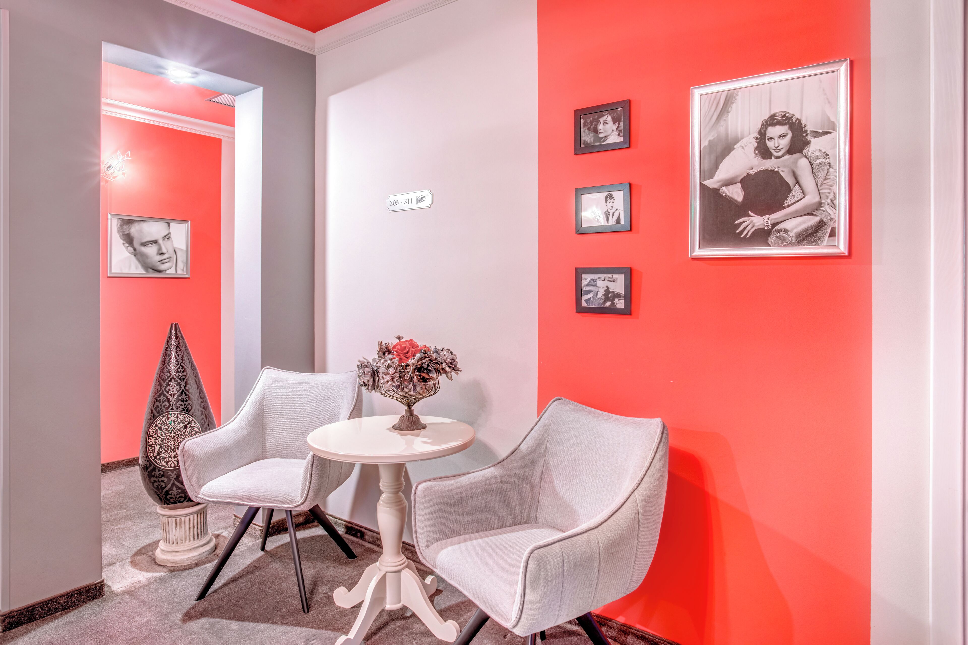 Un lobby moderno con una pared de acento rojo, una pequeña mesa redonda con un florero y dos sillones grises.