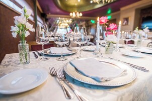 Una mesa de comedor dispuesta con platos, cubiertos y copas de vino, con un jarrón de flores y velas.