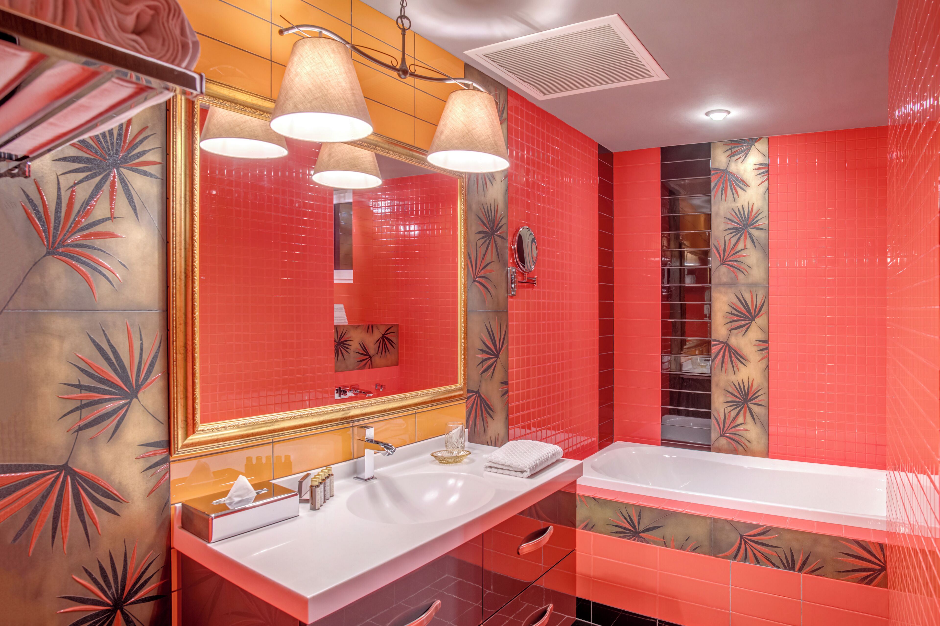 A modern bathroom with a red and gold color scheme, featuring a large mirror, two sinks, and a bathtub.