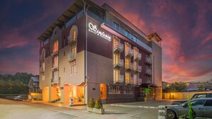 Um hotel com vários andares, varandas, uma placa com a inscrição 'Hotel & Restaurant' e uma área de estacionamento com carros.