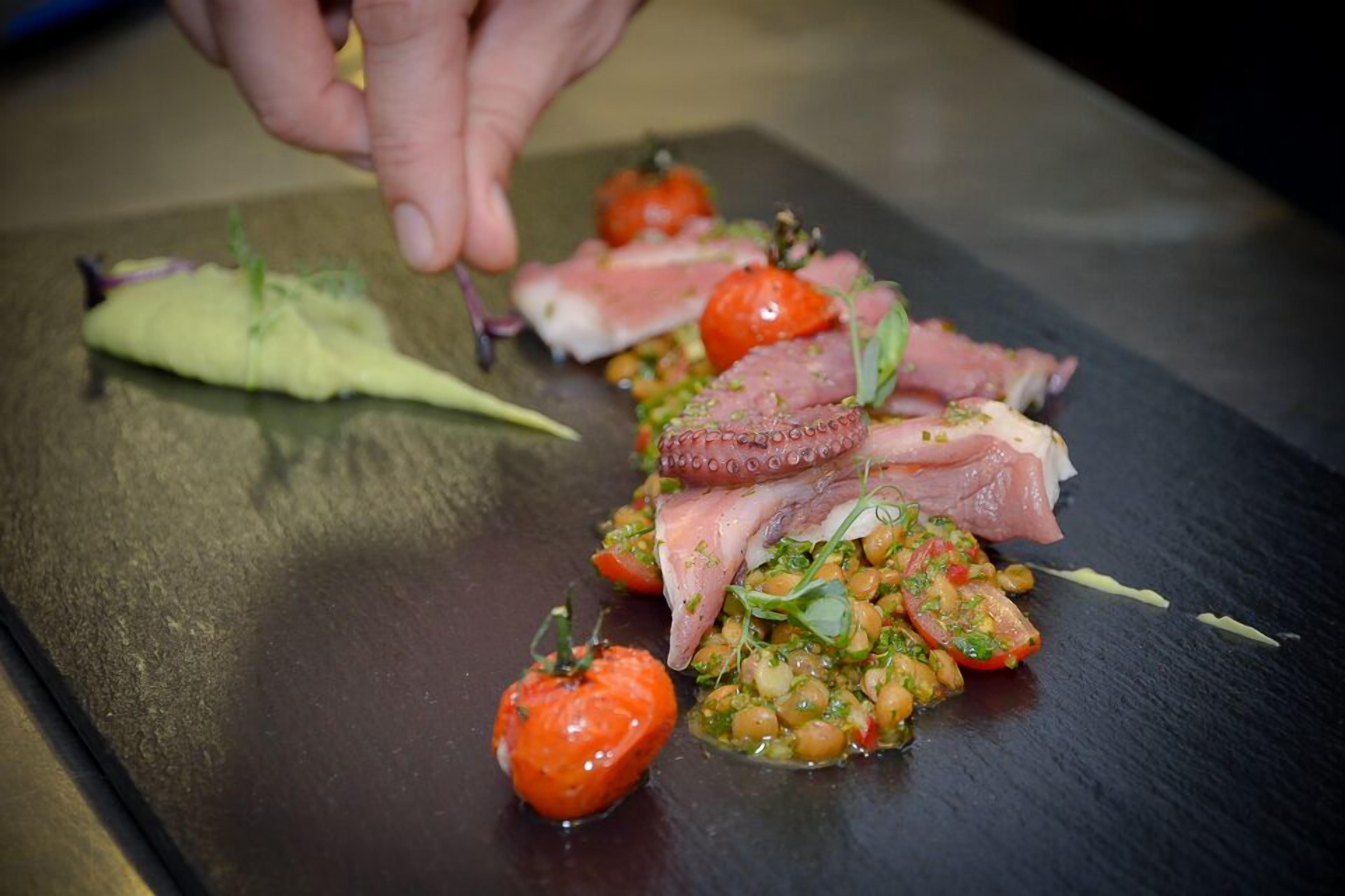 Un plato con pulpo, tomates y vegetales verdes sobre una pizarra.