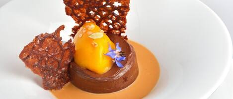 A dessert with a caramelized fruit and a chocolate sphere on a white plate.