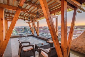 Un balcón de madera con muebles de mimbre y vista a la ciudad.