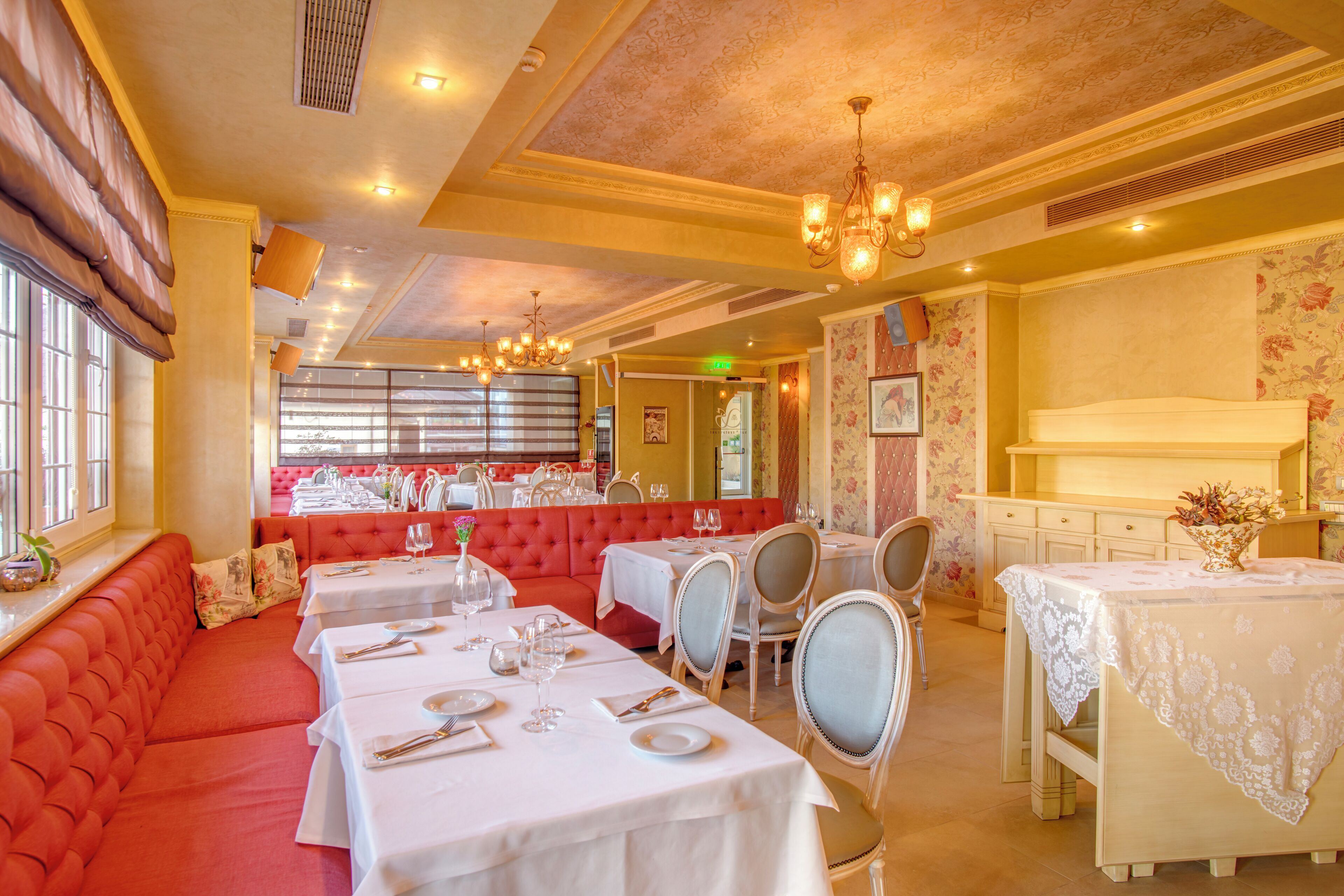 Restaurante com assentos acolchoados vermelhos, toalhas de mesa brancas e lustres.