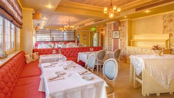 Restaurante com assentos acolchoados vermelhos, toalhas de mesa brancas e lustres.