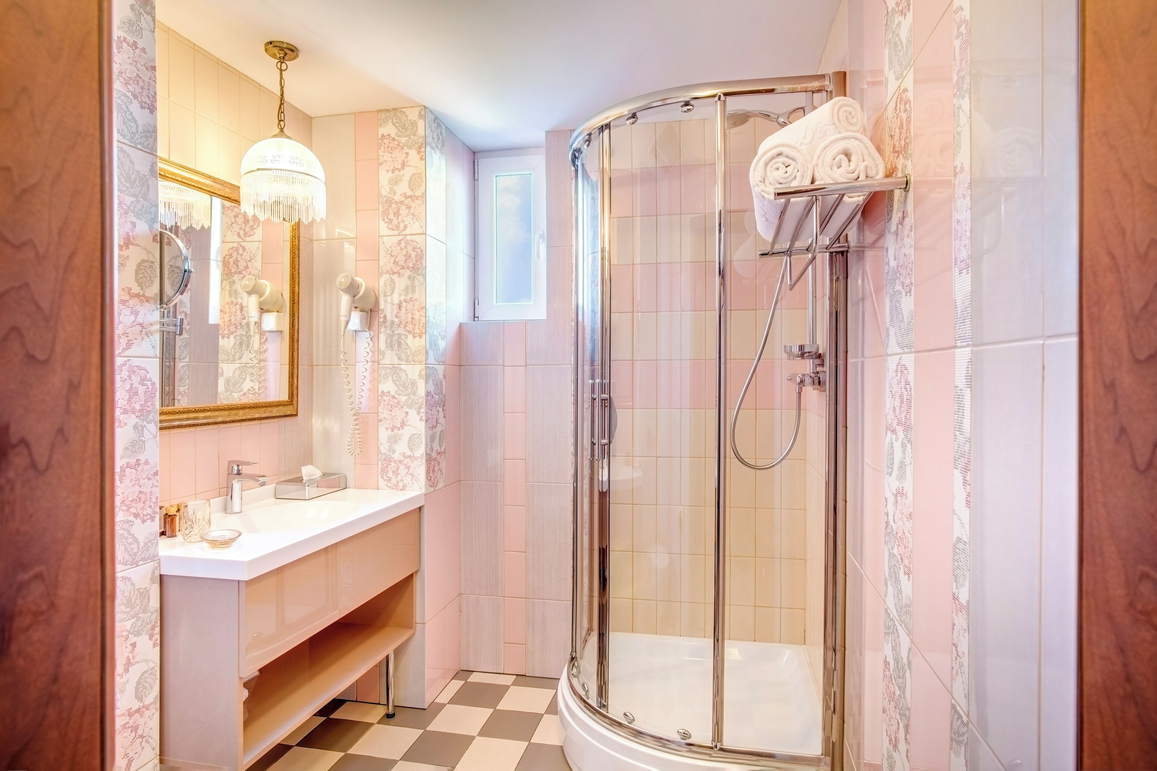 A bathroom with a glass-enclosed shower, a vanity with a mirror, and a chandelier.