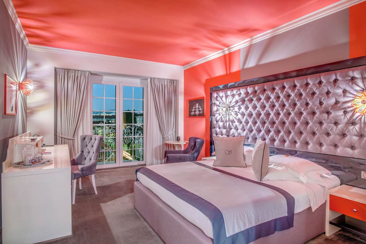 A modern bedroom with a large bed, a tufted headboard, and a view of the outdoors through a window with curtains.