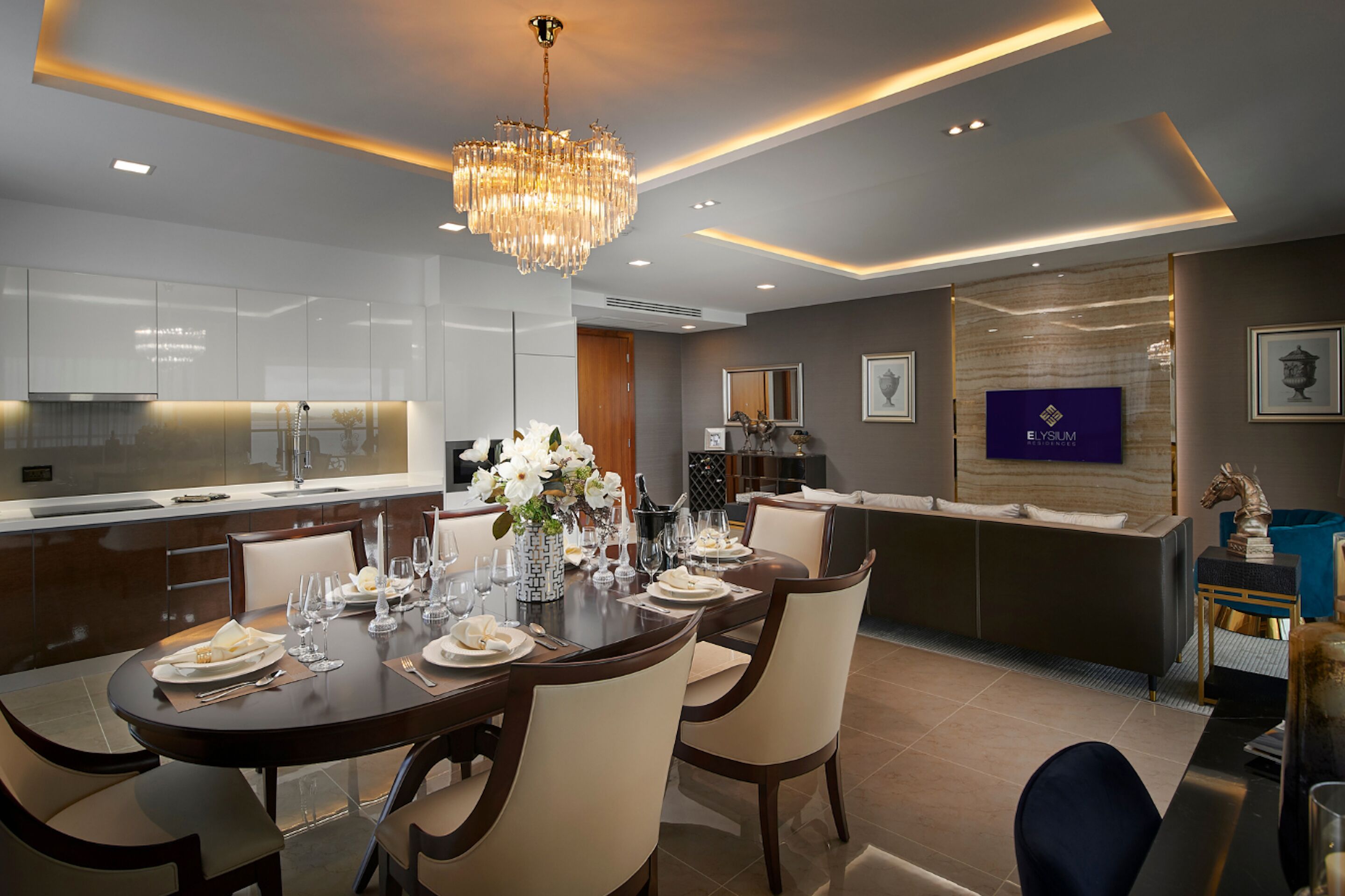 A modern dining area with a chandelier, a large table set for six, and a bar area with a television.